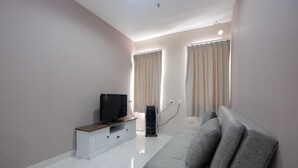 A modern living room with a flat-screen TV on a wooden stand, a grey sofa, and a white cabinet. - Relax 1BR Apartment at Sentul Tower (Citaringgul)