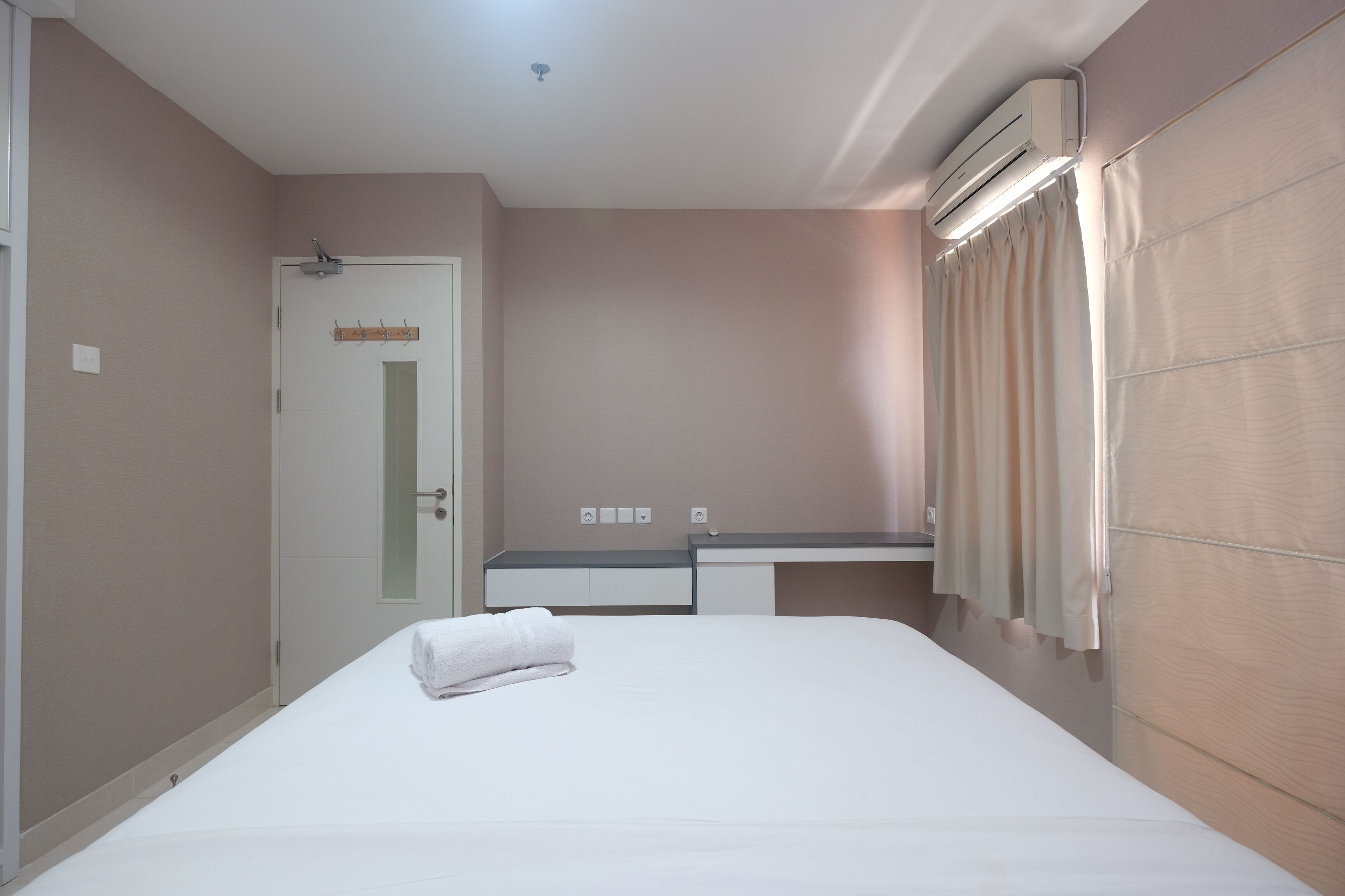 A hotel room with a bed, a desk, and an air conditioning unit.
