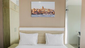 A neatly made bed with white linens and pillows, a wooden headboard, and a cityscape painting above it. - Compact and Cozy Studio Apartment Springwood Residence (Tangerang)