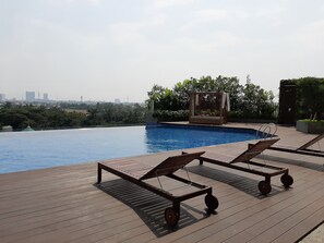 Relax by the rooftop pool with a stunning city view, surrounded by a deck and shaded seating area.
