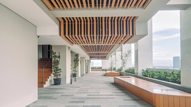 A spacious corridor with a wooden slatted ceiling, potted plants, and a long wooden bench. - Cozy and Elegant Studio The Smith Alam Sutera Apartment (Tangerang)