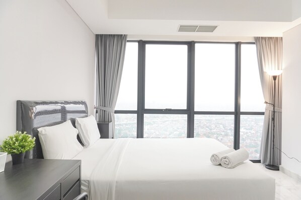 Un moderno cuarto de hotel con una cama grande, una mesita de noche con una planta y vistas a la ciudad a través de amplios ventanales.