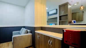 A modern room with a sofa, wooden cabinets, a coffee machine, and a built-in air conditioning unit. - Best Deal and Modern 1BR Sentul Tower Apartment (Citaringgul)