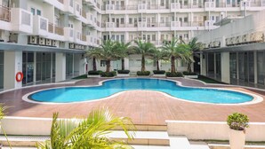 A multi-story hotel with a central swimming pool surrounded by palm trees and a brick deck. - Best Deal and Modern 1BR Sentul Tower Apartment (Citaringgul)