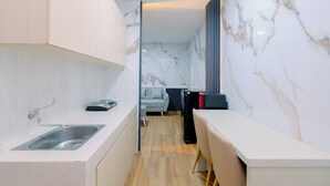 A modern kitchen with a built-in sink, a dining area with a table and chairs, and a living space with a sofa and a TV. - Restful and Modern 2BR at Sentul Tower Apartment (Citaringgul)