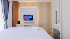 A modern hotel room with a large bed, a flat-screen TV mounted on a wall, a bedside table, and a small desk with a mirror. - Restful and Modern 2BR at Sentul Tower Apartment (Citaringgul)