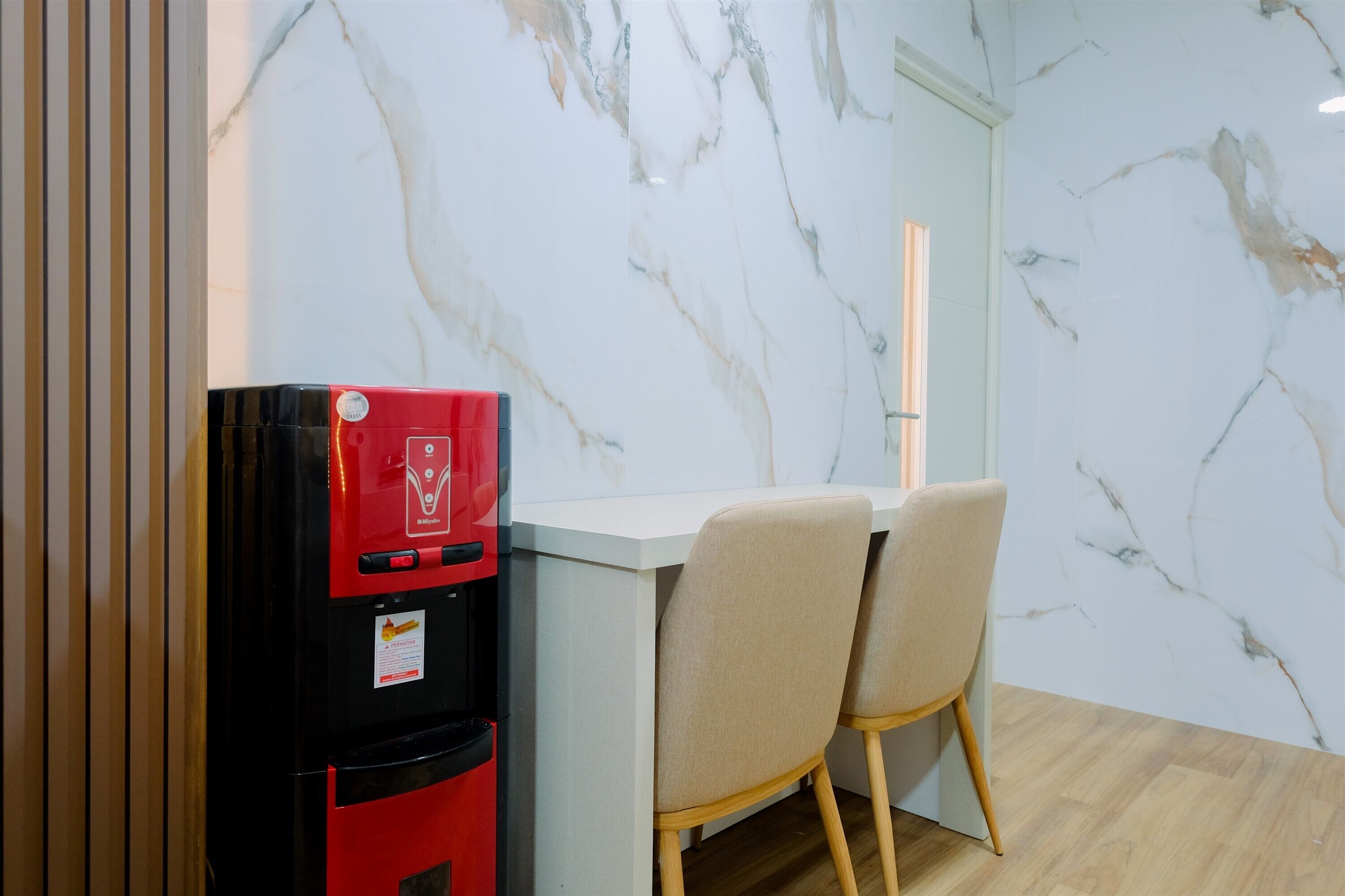 A compact kitchen with a marble backsplash, a red refrigerator, and two beige chairs.