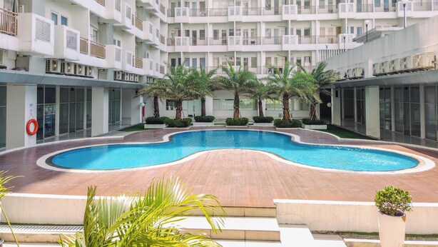 A multi-story hotel with a central swimming pool surrounded by palm trees and a brick deck. - Restful and Modern 2BR at Sentul Tower Apartment (Citaringgul)