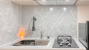 A modern kitchen with a marble backsplash, a built-in sink, a gas stove, and a ceiling light. - Cozy and Well Furnished Studio Grand Kamala Lagoon Apartment (Bekasi)