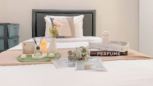 A neatly made bed with a white and gray pillow, a bouquet of flowers, a book titled 'The Kinfolk Entrepreneur', and a perfume box on a bedspread. - Cozy and Well Furnished Studio Grand Kamala Lagoon Apartment (Bekasi)