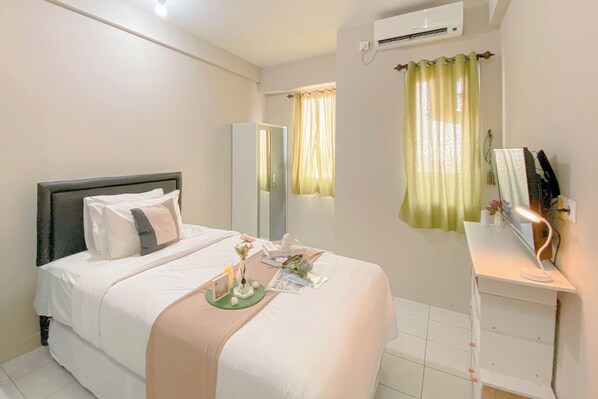 A neatly arranged bedroom with a bed, bedside table, mirror, and a window with curtains. - Cozy and Well Furnished Studio Grand Kamala Lagoon Apartment (Bekasi)