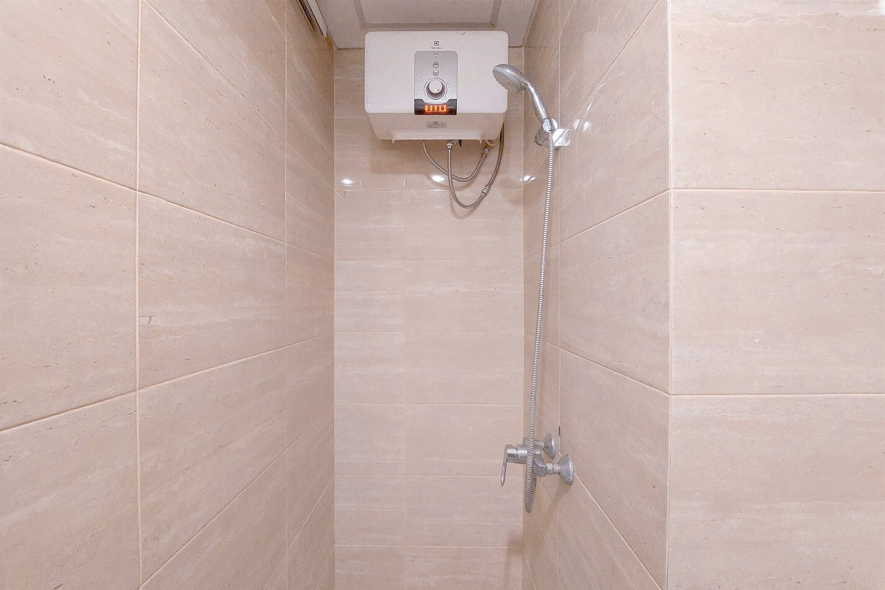 Un petit espace de douche carrelé, doté d’un chauffage intégré et d’un pommeau de douche amovible.