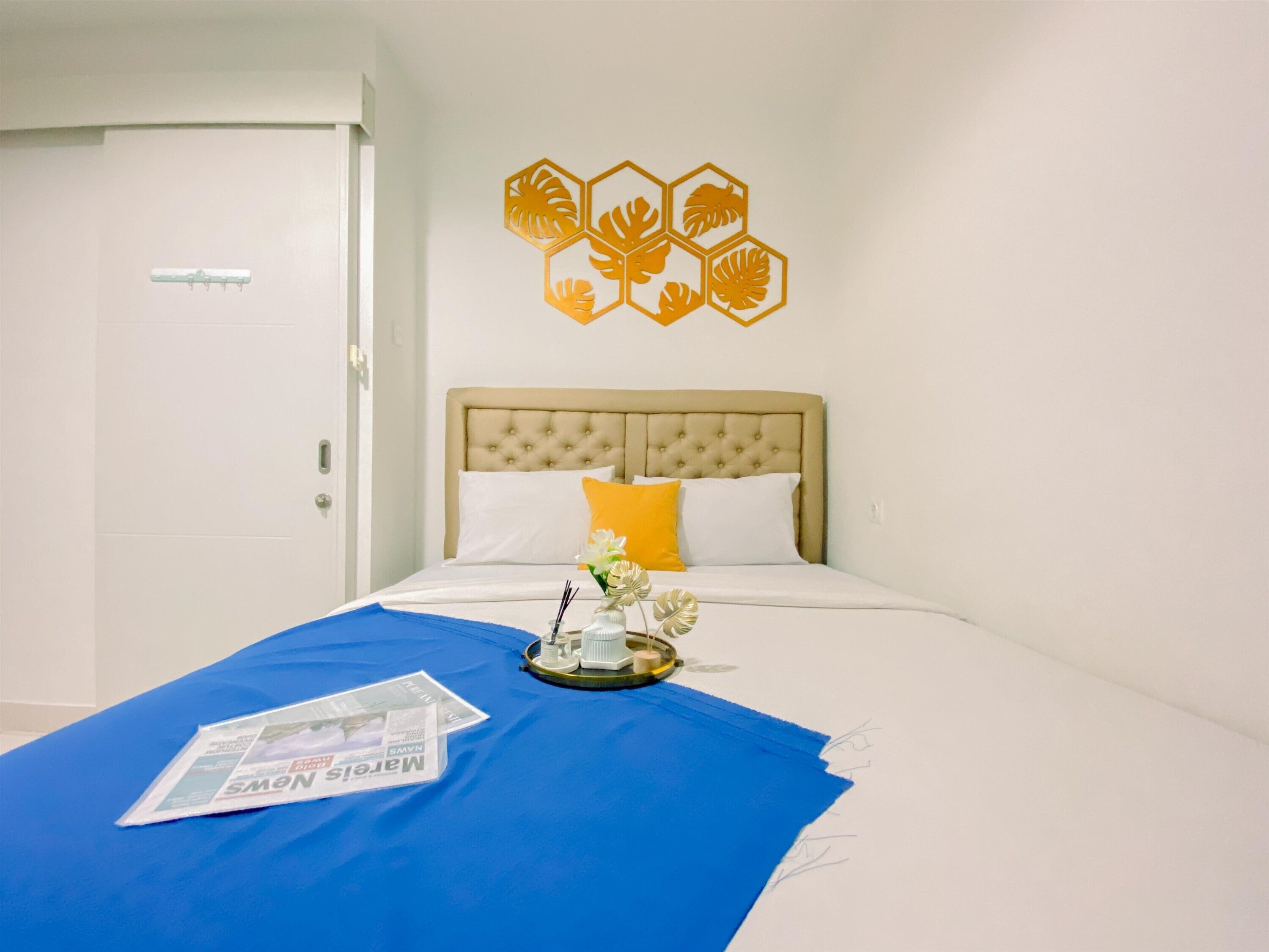 Una habitación de hotel con una cama, una manta azul, un periódico y un adorno en la pared.