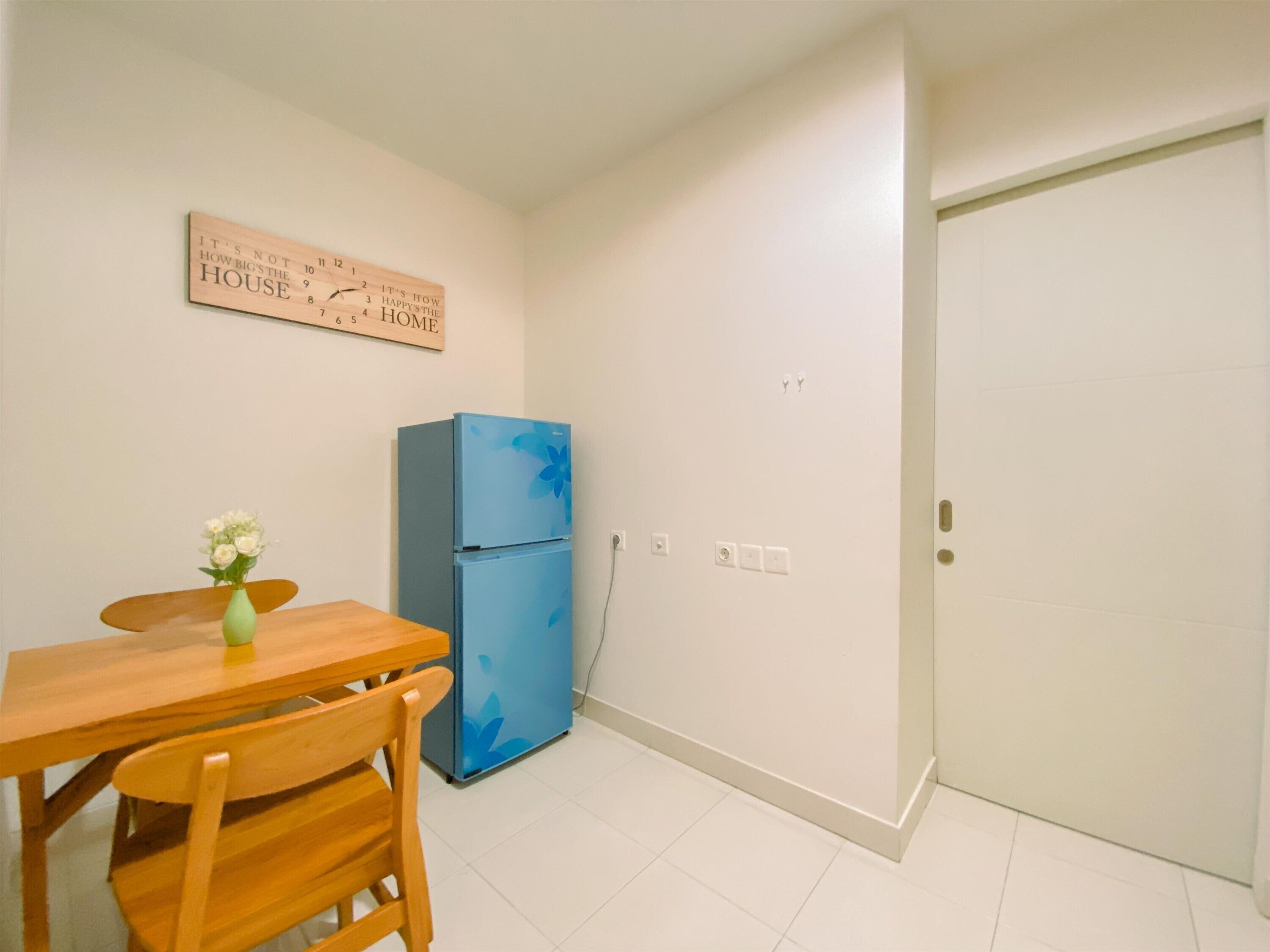 A small kitchen with a wooden table and chairs, a blue refrigerator, and a wall clock.