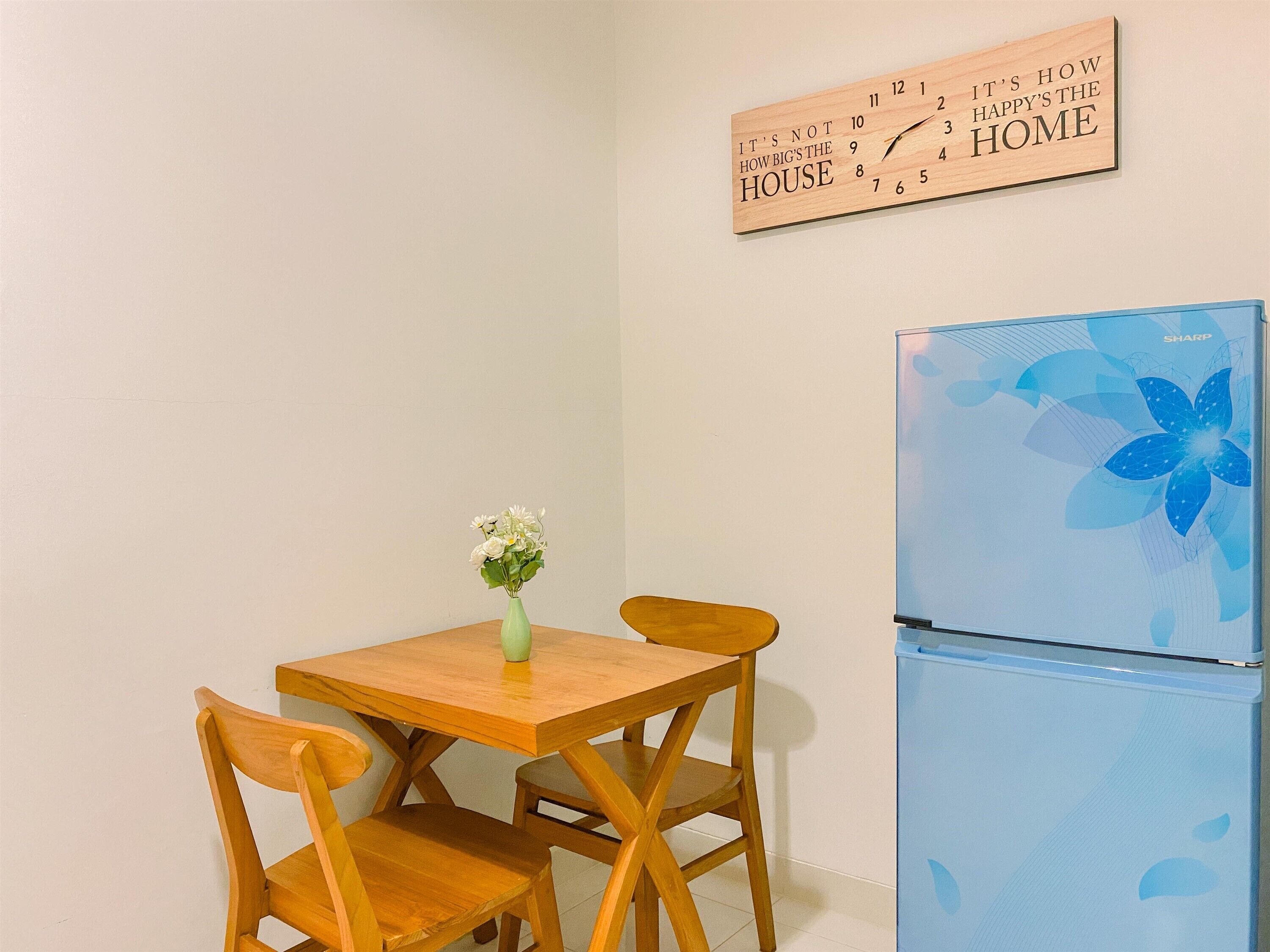 A small kitchen with a wooden table and chairs, a blue refrigerator, and a wall clock.