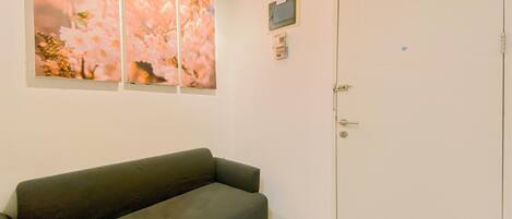 A room with a dark-colored sofa, a white door, and a wall-mounted telephone.