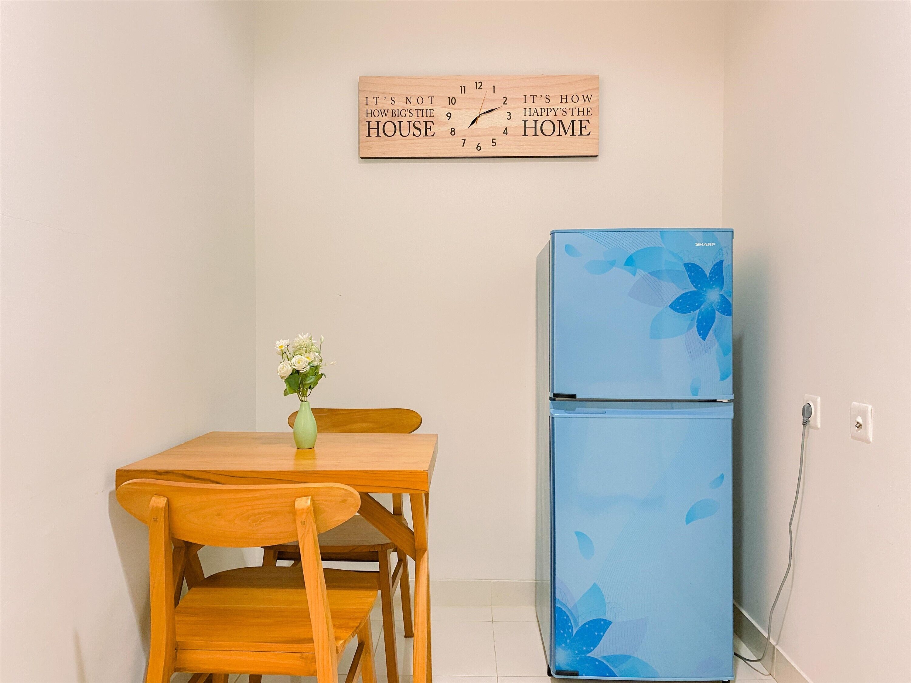 A small kitchen with a wooden table and chairs, a blue refrigerator, and a wall clock.