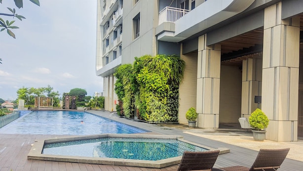 A swimming pool with lounge chairs, surrounded by a wooden deck and a building with a balcony. - Modern Look Studio at Springwood Residence Tangerang Apartment (Tangerang)
