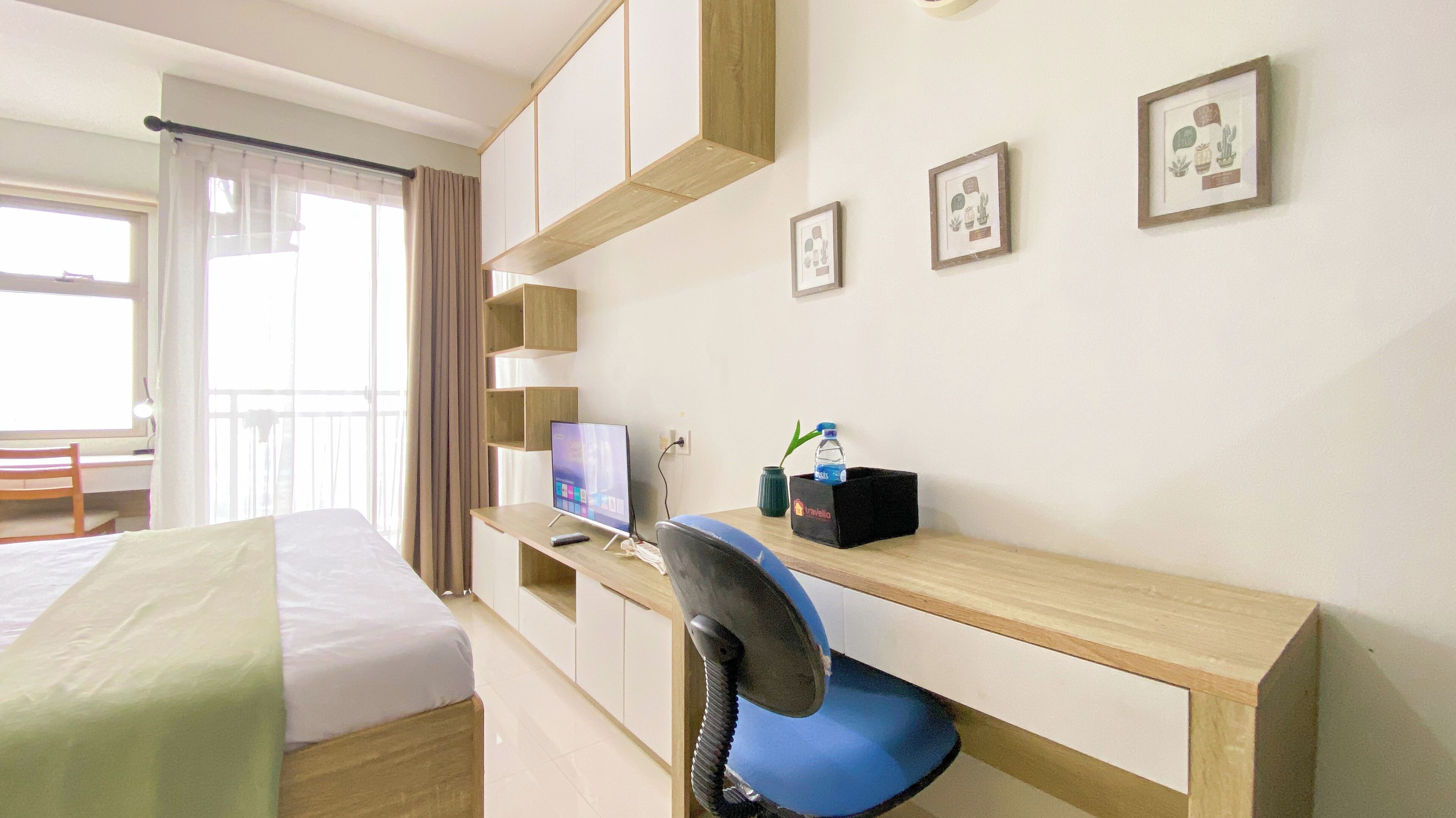 A hotel room with a bed, a desk with a computer, a chair, and a window with curtains.