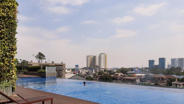 A rooftop pool with lounge chairs, a cityscape view, and high-rise buildings in the background. - Modern Look and Restful Studio Apartment Springwood Residence Tangerang (Tangerang)