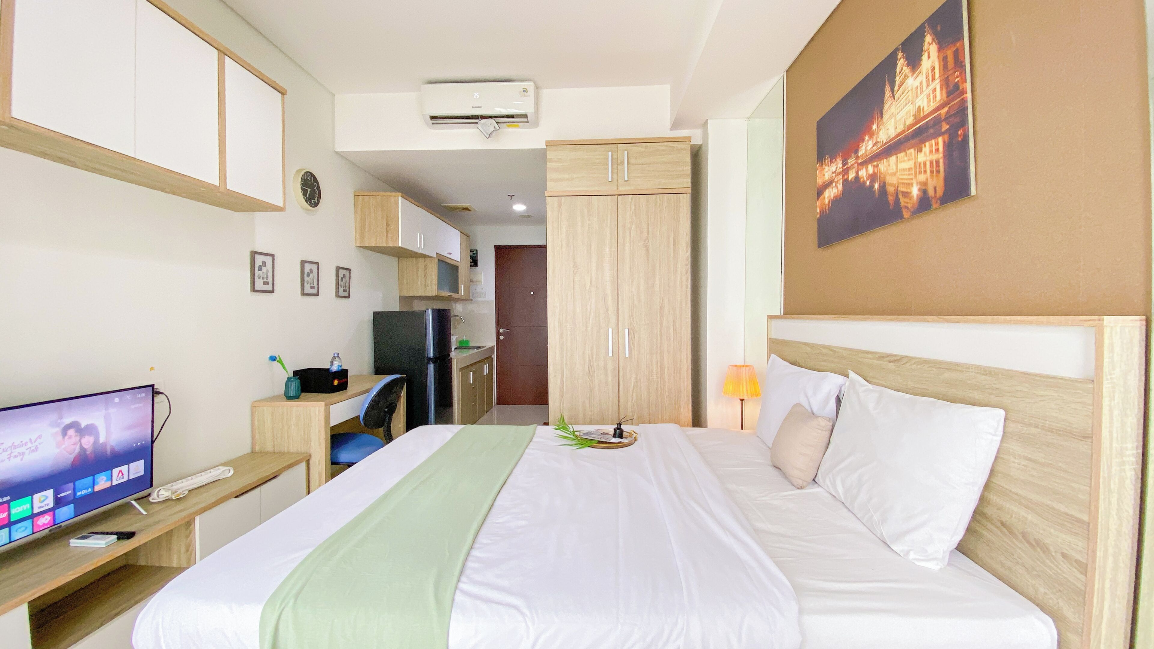 A hotel room with a bed, a desk with a computer, a television, and a kitchenette.