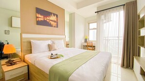 A hotel room with a large bed, a bedside table with a lamp, a chair, a desk, and a window with curtains. - Modern Look and Restful Studio Apartment Springwood Residence Tangerang (Tangerang)