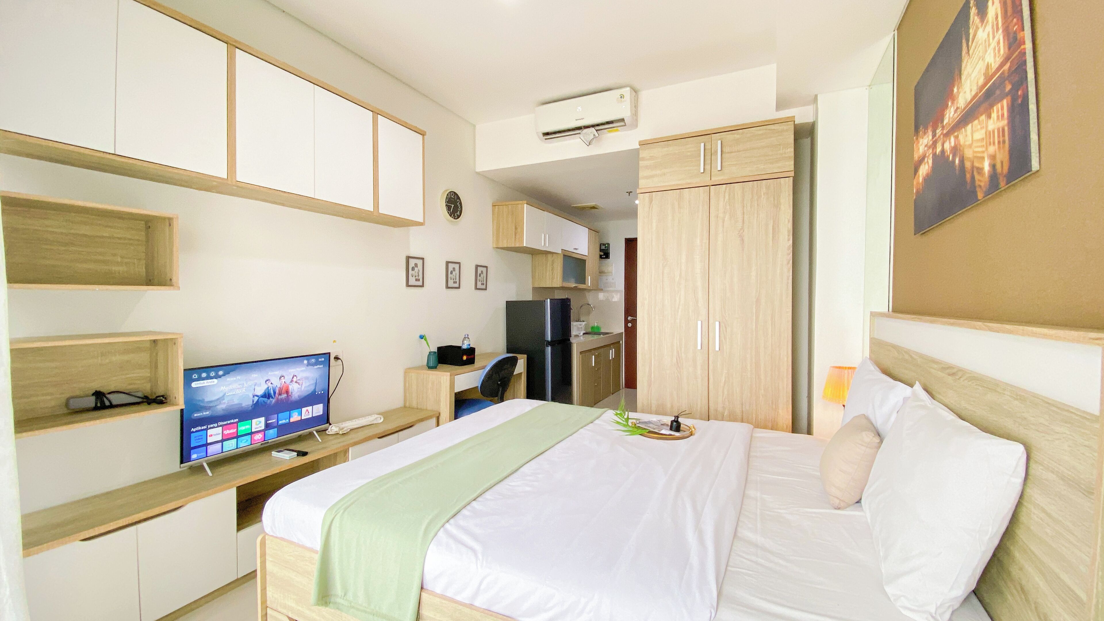 A hotel room with a bed, a desk with a computer, a television, a refrigerator, and a wardrobe.
