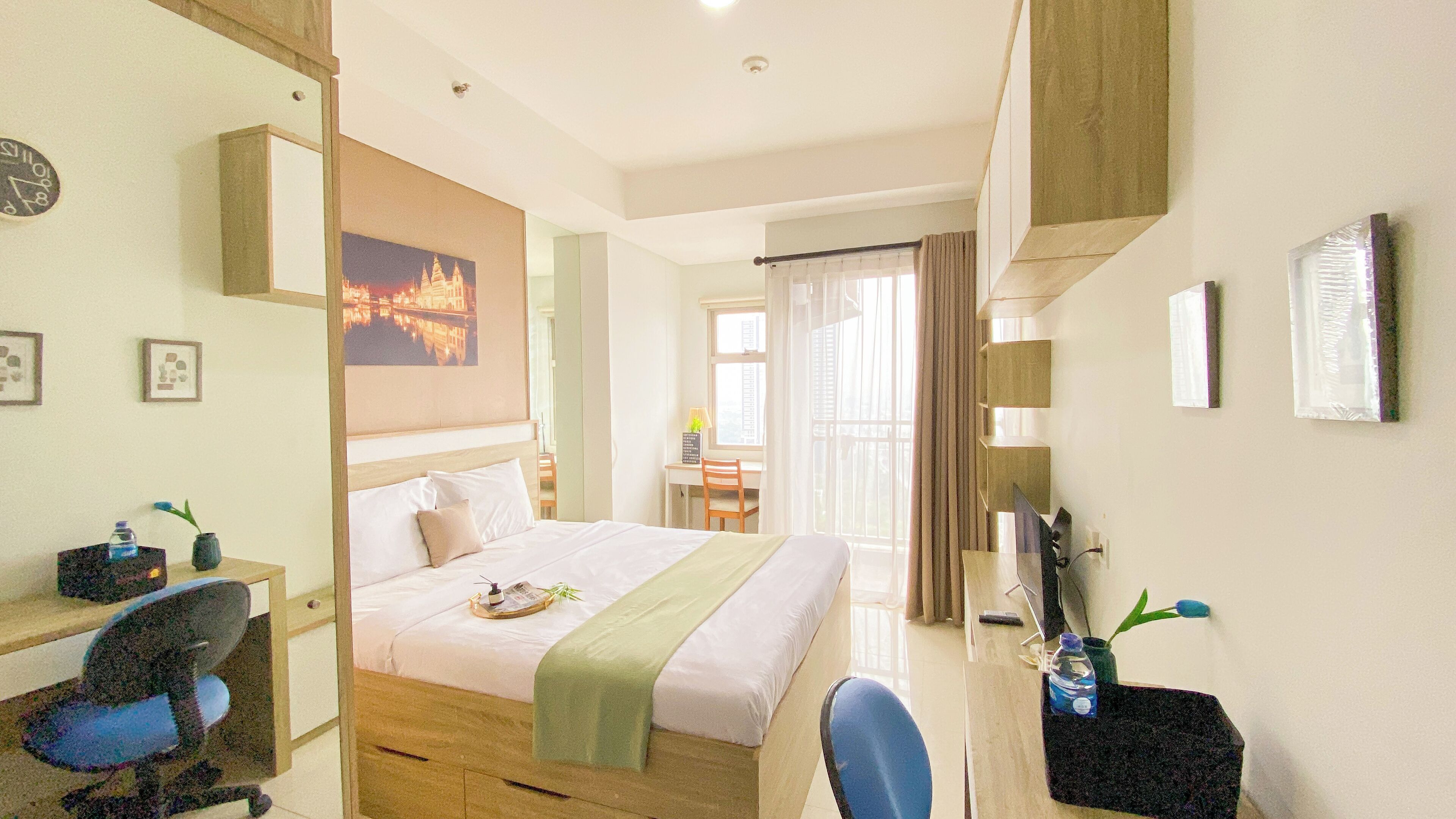 A hotel room with a bed, desk, chair, and a view of a building through the window.
