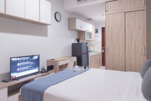 Ett hotellrum med en säng, ett skrivbord med en dator, en tv som visar nyheter, en klocka och en garderob.