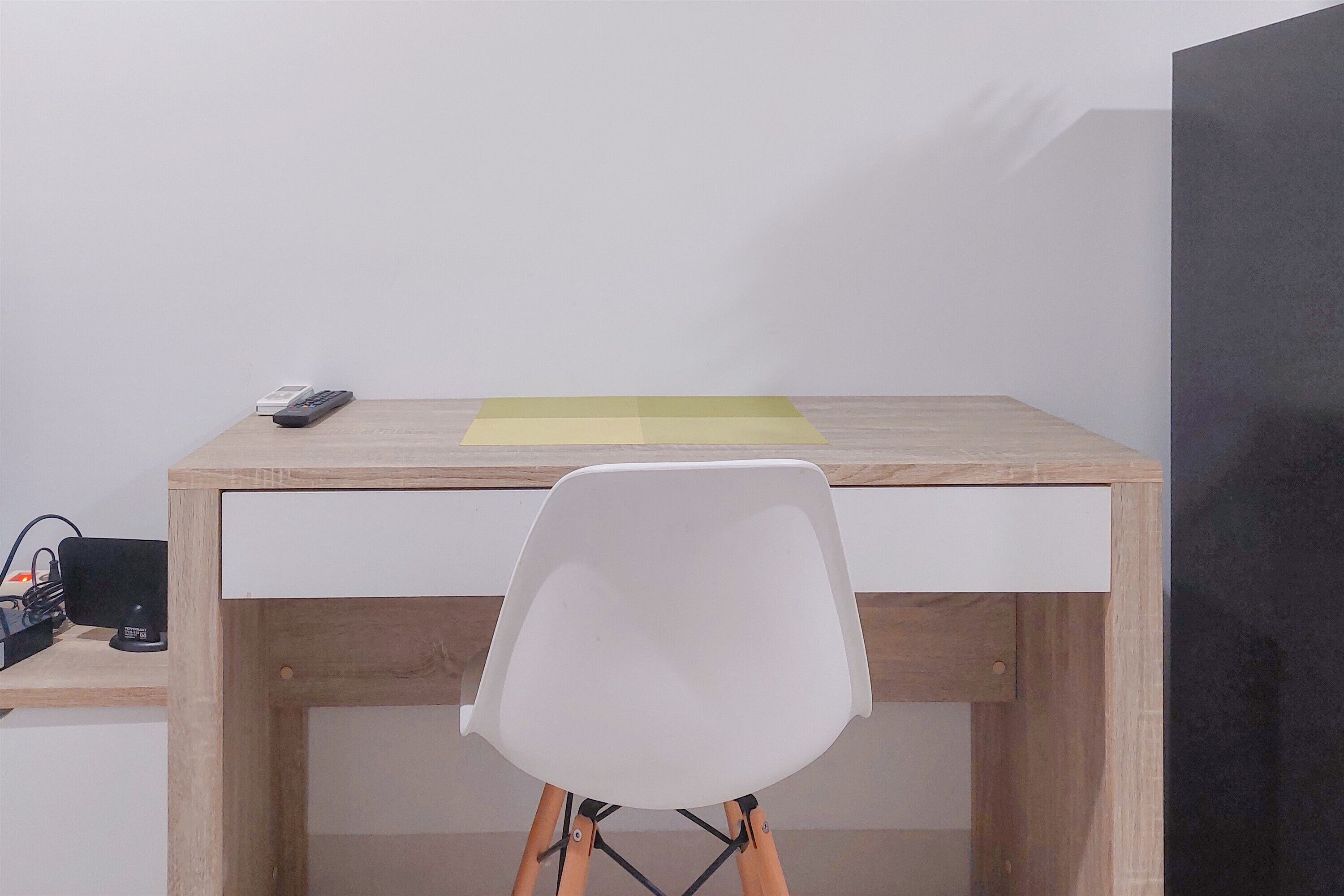 A wooden desk with a white chair, a remote control, and a yellow sticky note.