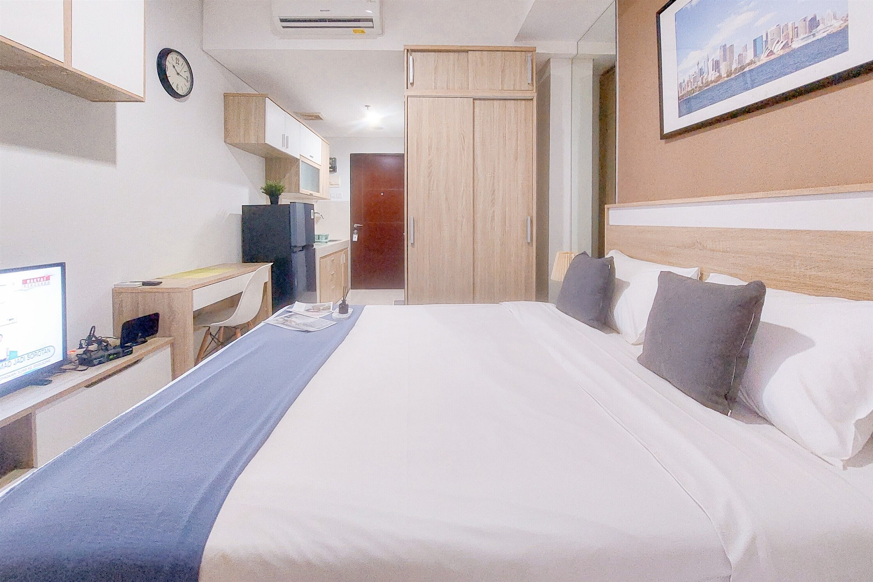 A hotel room with a bed, a desk, a chair, a television, a wardrobe, and a picture on the wall.