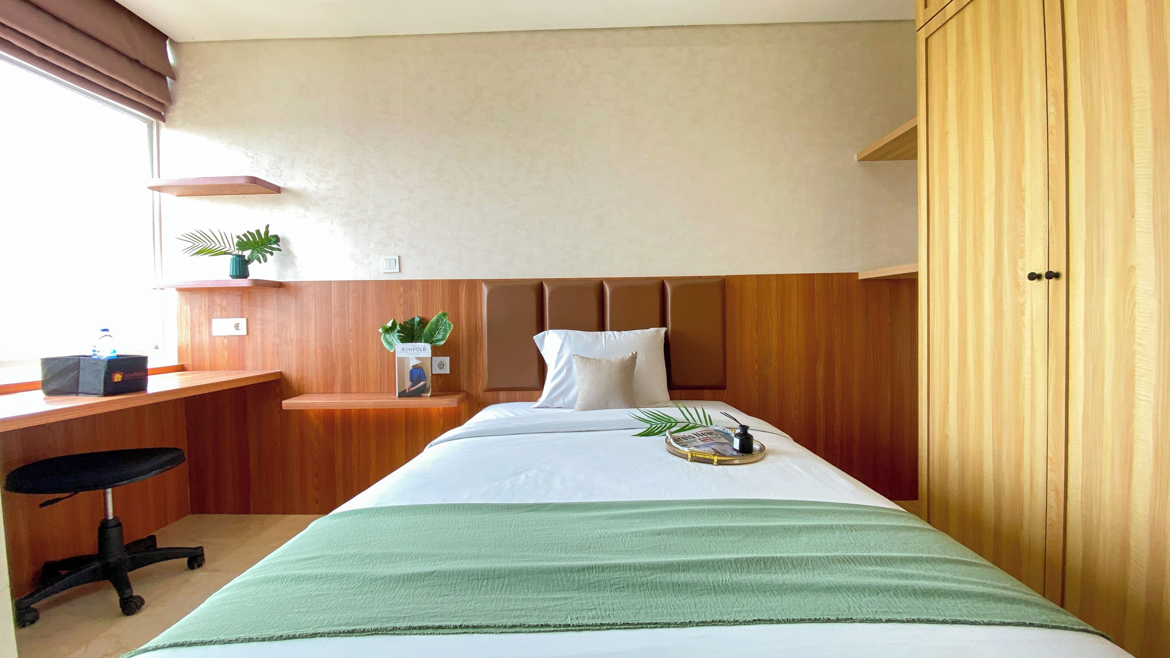 A hotel room with a bed, a desk, a chair, a wardrobe, and a potted plant.