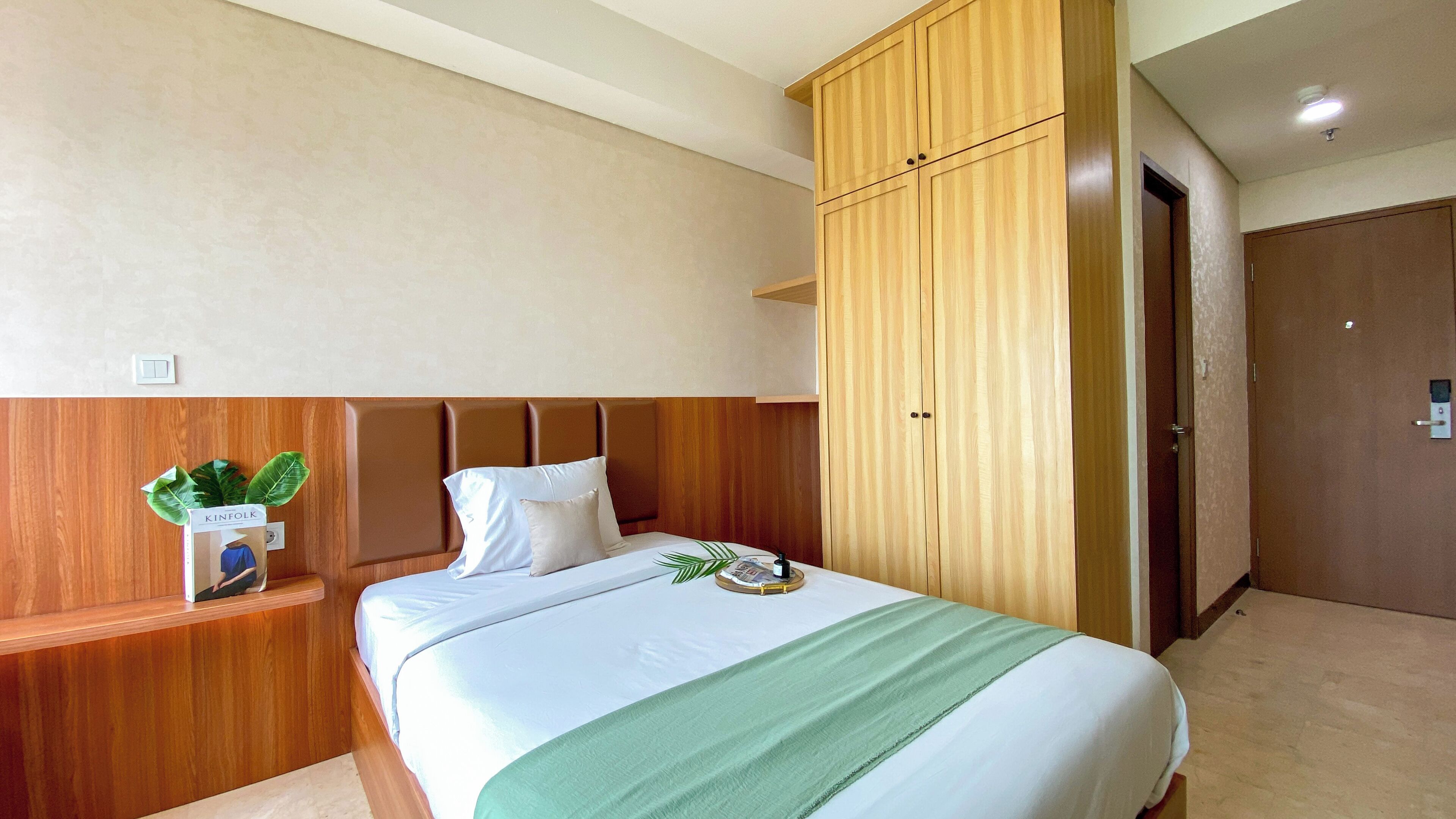 Une chambre d’hôtel avec un grand lit, une tête de lit en bois, une table de chevet avec une plante et une armoire.