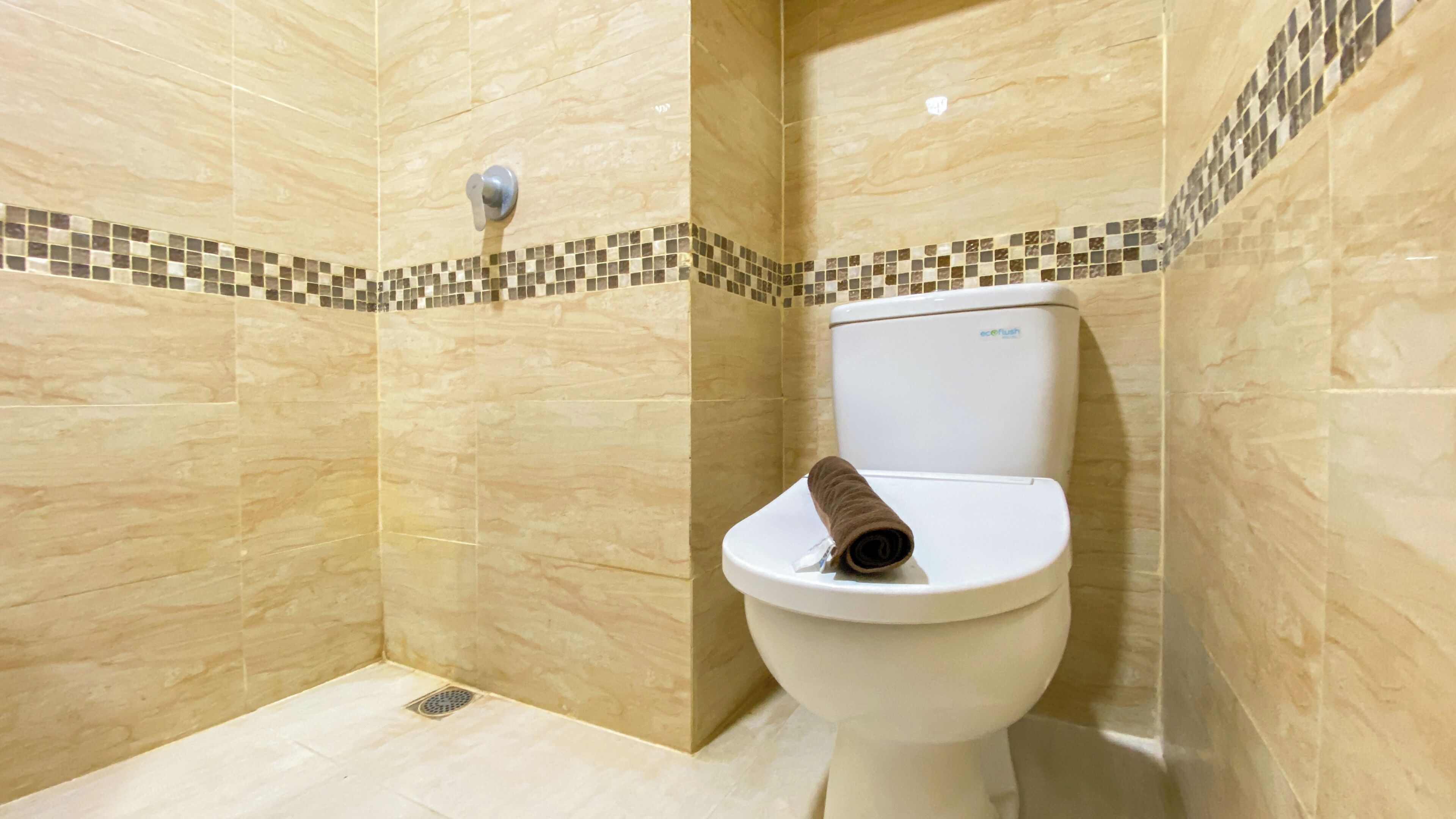 Une salle de bain avec des carreaux de couleur beige, des toilettes blanches et un petit espace douche.