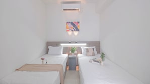 A modern hotel room with two single beds, a bedside table with a lamp, a small plant, and a colorful abstract painting on the wall.