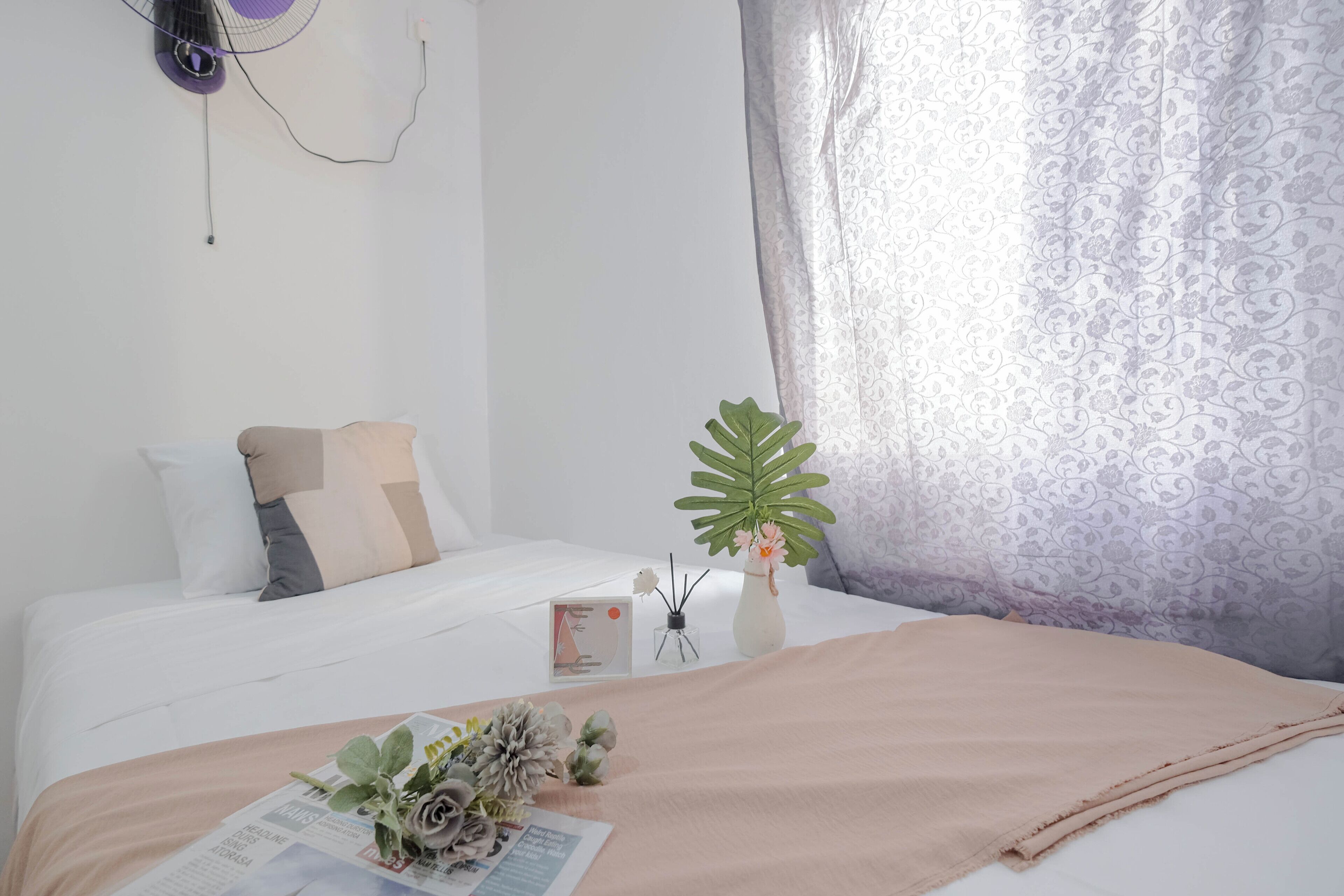 A neatly made bed with a beige blanket, a white pillow, and a decorative plant on the side.