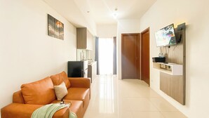 A living room with a brown sofa, a flat-screen TV mounted on the wall, and a kitchen area in the background. - Stunning and Well Designed 2BR Apartment at Vittoria Residence (Jakarta)
