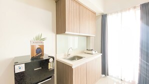 A modern kitchen with a black countertop, a stainless steel sink, wooden cabinets, and a window with curtains. - Stunning and Well Designed 2BR Apartment at Vittoria Residence (Jakarta)