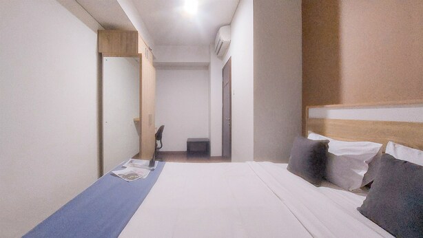 A hotel room with a bed, a blue towel, a chair, and a small table. - Good Deal and Homey 1BR Apartment Springwood Residence Tangerang (Tangerang)