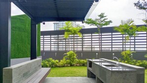 A modern outdoor patio with a concrete sink and bench, surrounded by greenery and a view of buildings. - Spacious and Homey 2BR at Podomoro City Deli Medan Apartment (Medan)