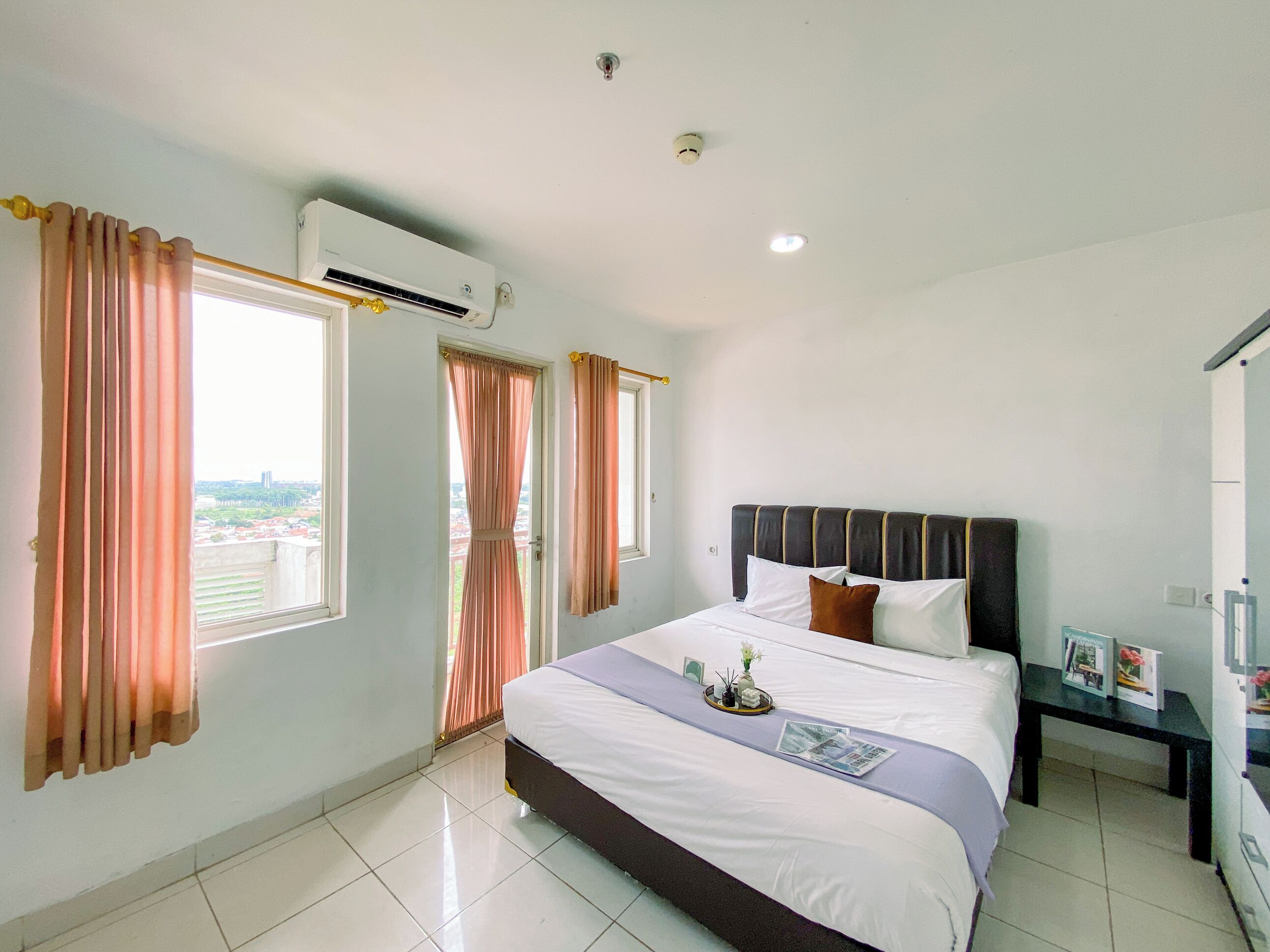 A hotel room with a large bed, a bedside table with a lamp, and a window with curtains.