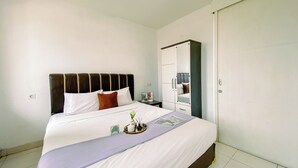 Ein ordentlich bezogenes Bett mit Kopfteil, ein Nachttisch mit Lampe und ein Schrank mit Spiegel.