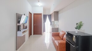 A modern living room with a TV, a sofa, a refrigerator, and a kitchen area with a sink and cabinets. - Best Deal and Stunning 2BR Apartment at Vittoria Residence (Jakarta)