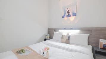 Een hotelkamer met een net opgemaakt bed, een nachtkastje met een boek, en een luchtverkoeler aan de muur.