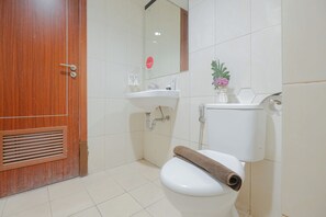 Ein Badezimmer mit Holztür, weißen Fliesen, einem Waschbecken, einer Toilette mit Handtuch und einem Spiegel.