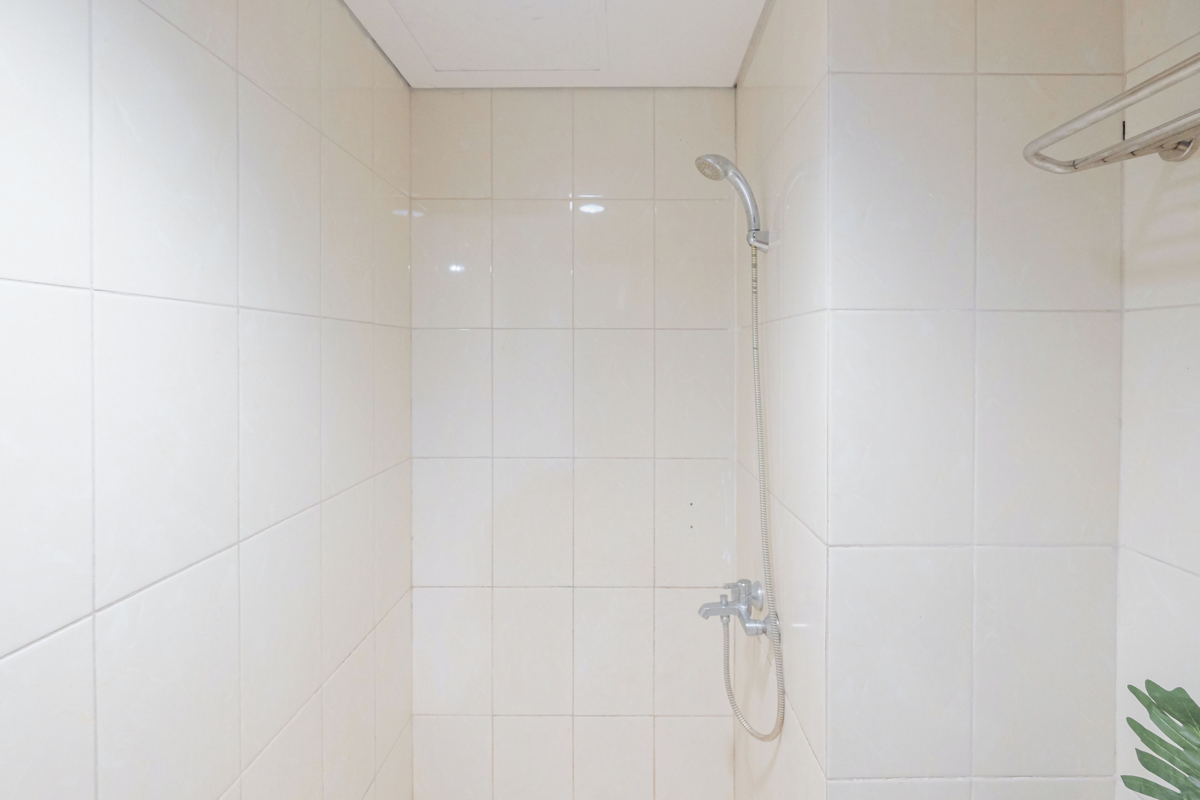 Eine kleine, geflieste Duschkabine mit einer Handbrause und einem am Wand montierten Wasserhahn.