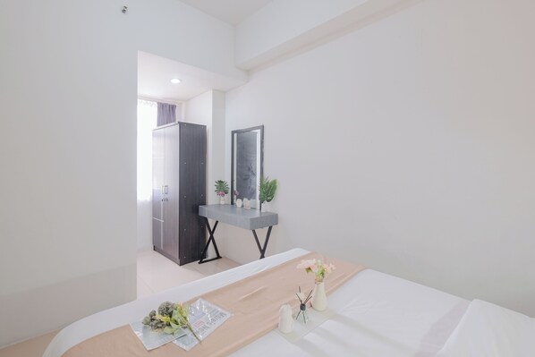 Une chambre d’hôtel moderne, équipée d’un lit, d’une table de chevet avec un miroir et d’un petit bureau agrémenté d’une plante.