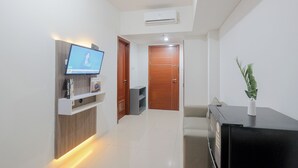A modern living room with a flat-screen TV, a built-in shelf, a black entertainment unit, and a potted plant. - Cozy and Sweet 2BR Apartment at Vittoria Residence (Jakarta)