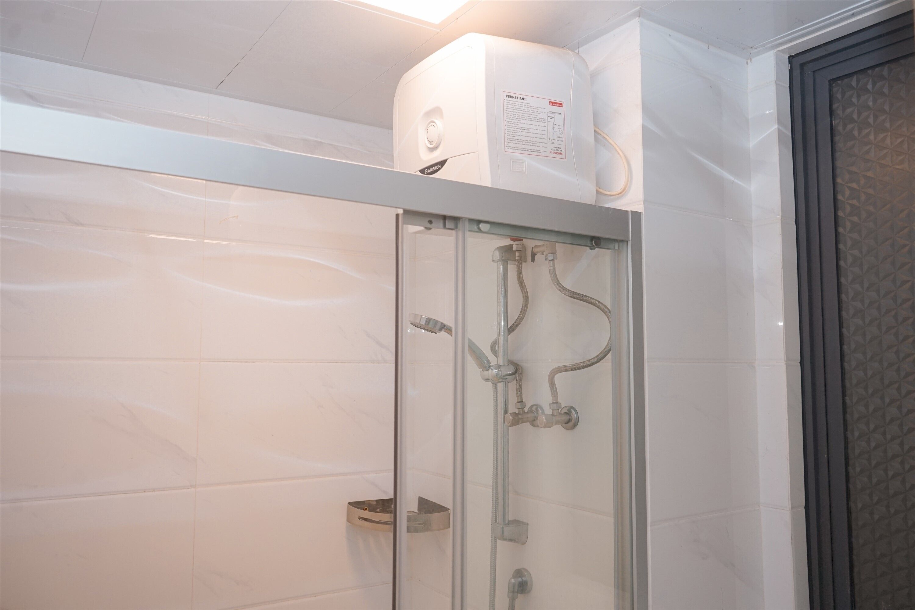 Una cabina doccia con pareti in ceramica bianca, un pannello comandi sopra e una mensola in metallo.