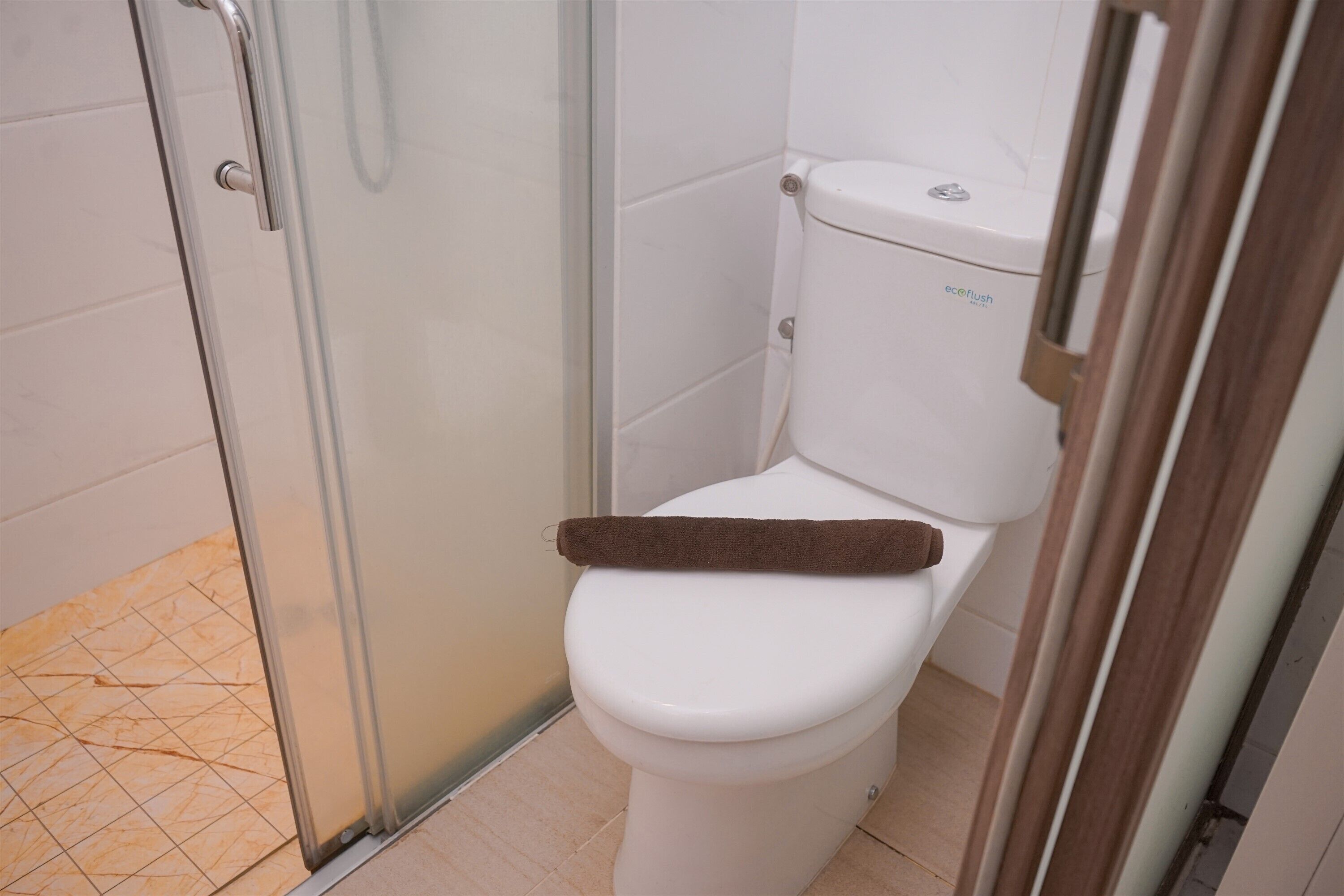 Un baño con inodoro blanco, cabina de ducha de vidrio y piso de baldosas.